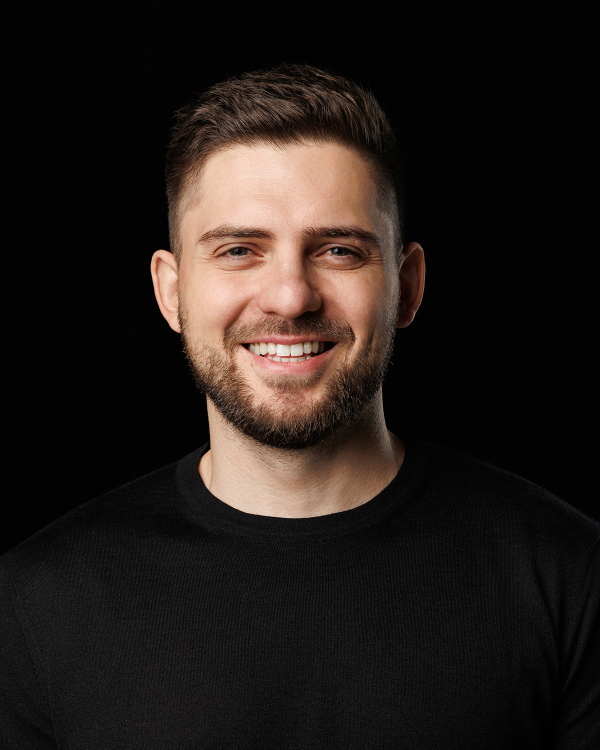 Pavlo Kharmanskyi — portrait, smiling, black sweater against a dark ground